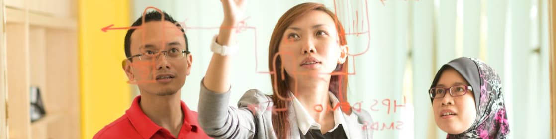 Colleagues gathered standing and discussing metrics on a glass board