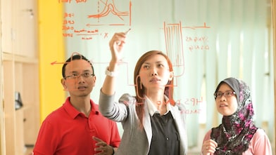 Colleagues gathered standing and discussing metrics on a glass board