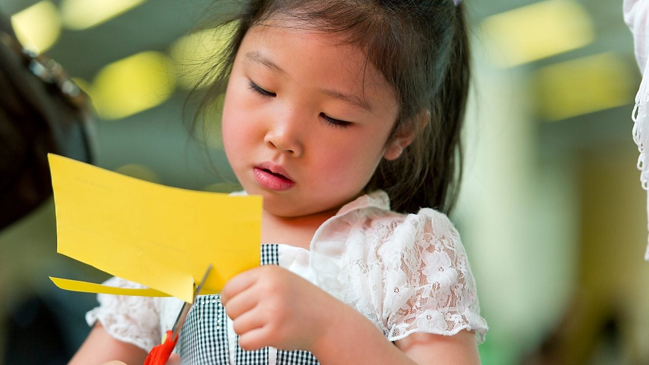 Young girl cutting paper with scissors.