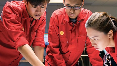 Diverse employees standing discussing while one is writing on the glass board.