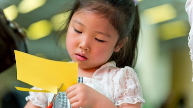 Young girl cutting paper with scissors.