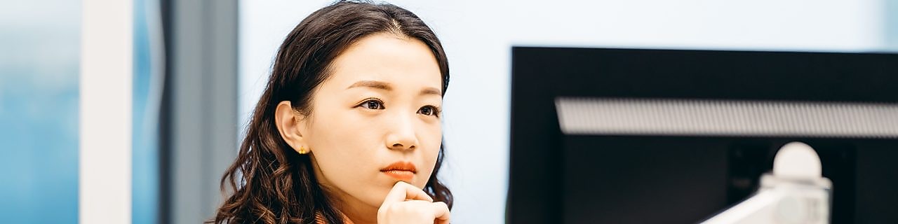 Person in formal business attire working at a desk, looking at a computer monitor in a modern office setting.