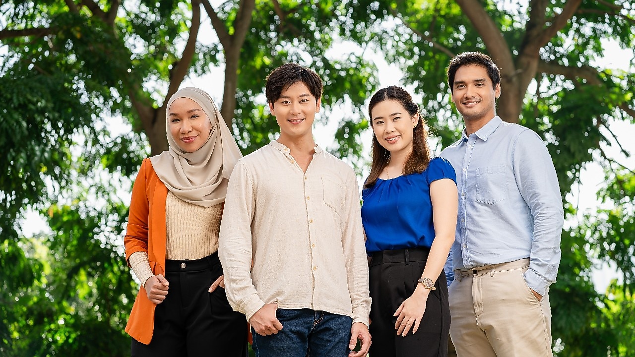 Group of four professionals standing outdoors under green trees, dressed in business casual attire.