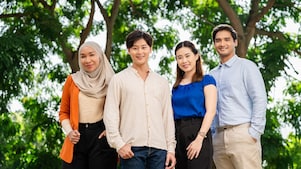 Group of four professionals standing outdoors under green trees, dressed in business casual attire.