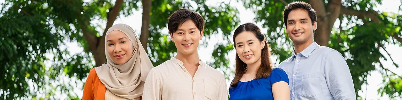Group of four professionals standing outdoors under green trees, dressed in business casual attire.