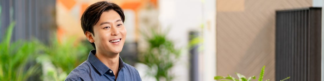 Person seated at a wooden table using a laptop, with a smartphone and potted plants in a bright modern workspace.