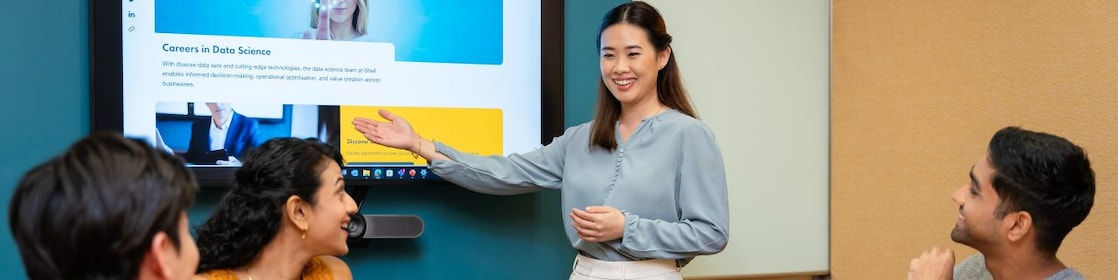 Person presenting a website on a large screen to three colleagues seated at a conference table with laptops and notebooks.