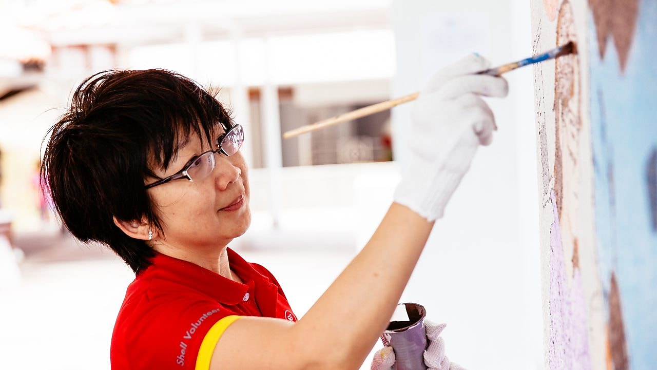 Shell volunteer Christine Low hard at work – and play – in painting one of the murals.