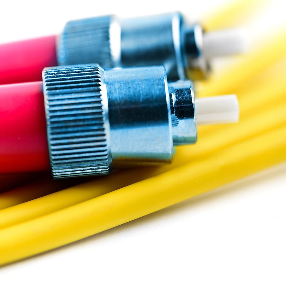 The two connector ends of an optical cable link sitting on some other yellow cable