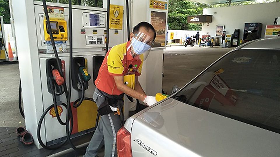 Pump attendant refueling car in face mask and shield